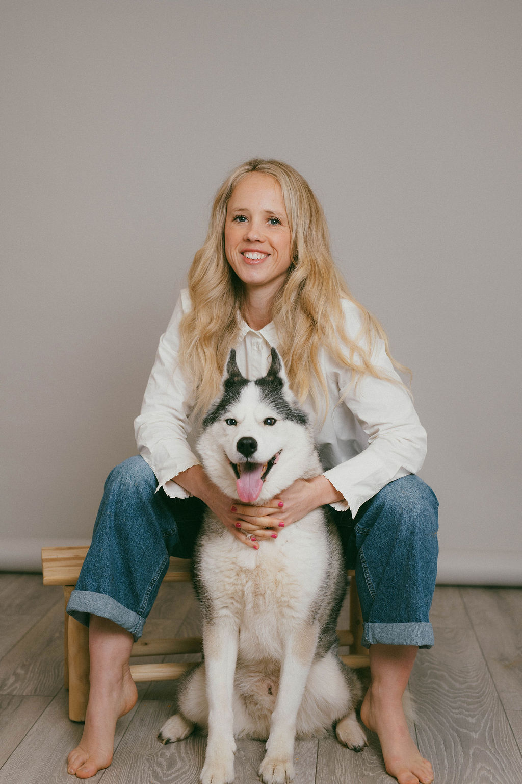 Kiri sitting on a bench with her husky between her legs in a studio portrait